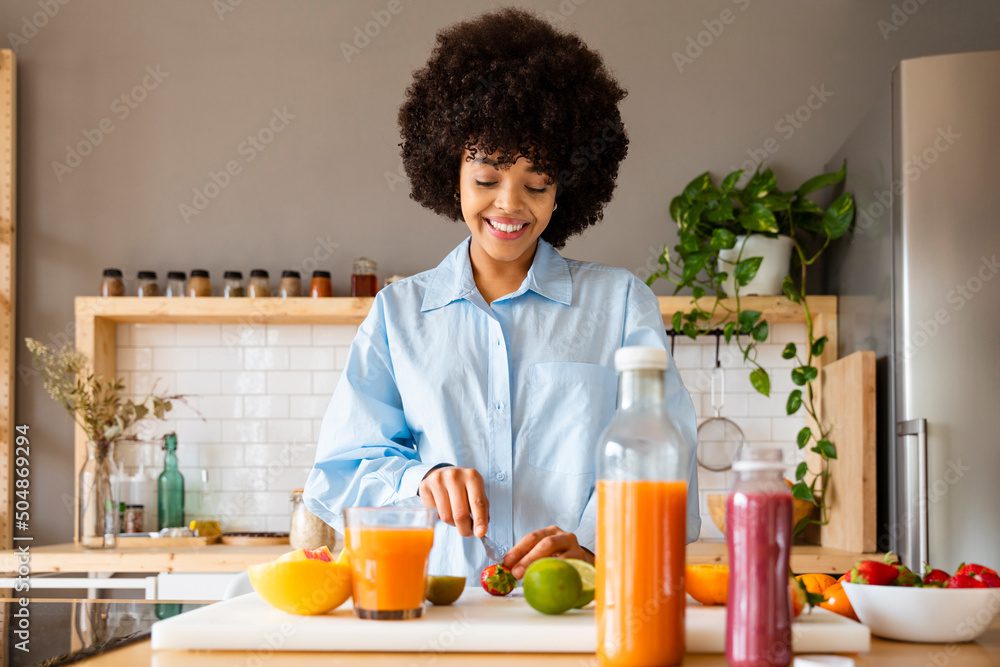 Beautiful woman cutting fruit with knife on board in kitchen at home