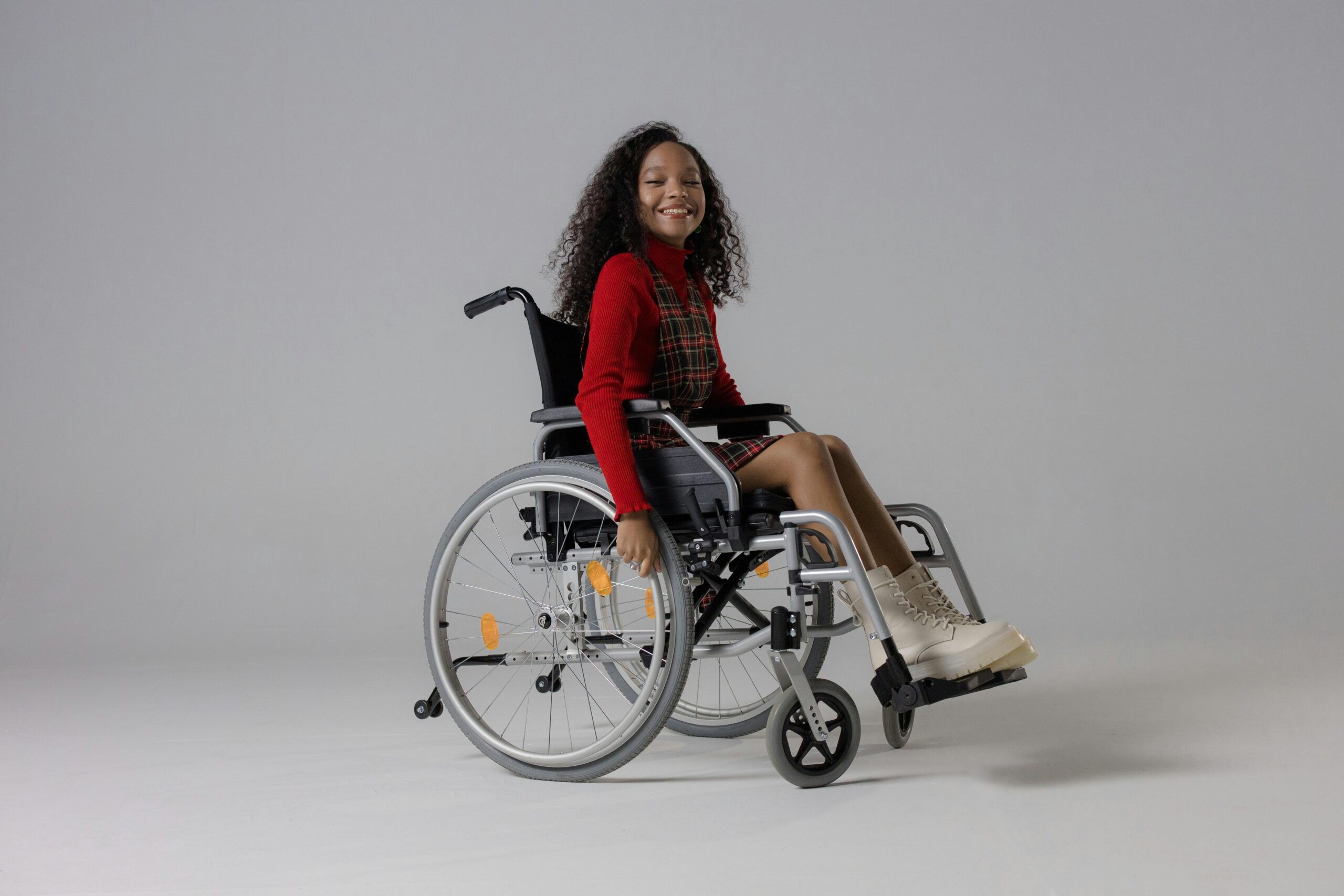 Girl in Red Sleeve Shirt Sitting in Wheelchair and Smiling